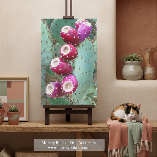 Santa Rita Arizona purple prickly pear cactus by Murray Bolesta! A framed art print of a prickly pear cactus with bright magenta-purple fruit hanging from a green cactus pad, displayed on a wooden stand in a styled room setting with a cat resting nearby.