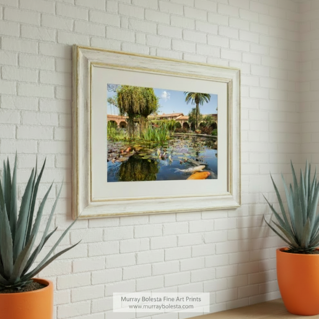 A tranquil pond with lily pads, surrounded by palm trees and a building with arched windows, creating a picturesque scene. San Juan Capistrano Mission Artwork - California Church Print by Murray Bolesta