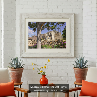 a stone church with two bells hanging from its side, surrounded by a stone wall and lush greenery. San Juan Capistrano Mission Wall Art - California Church Print by Murray Bolesta