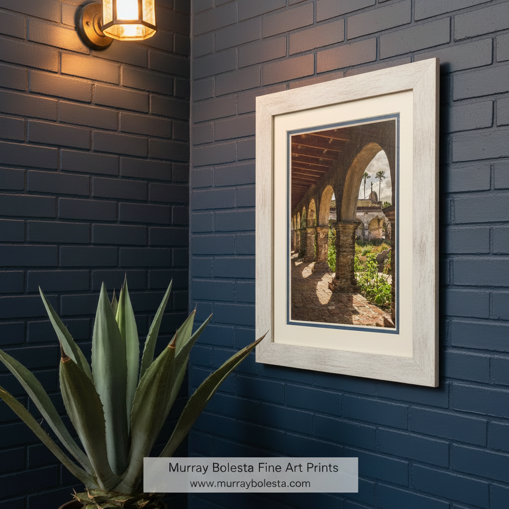 a covered walkway with arched columns, leading to a building with a dome and palm trees in the background. San Juan Capistrano Mission Art - California Historic Church Print by Murray Bolesta