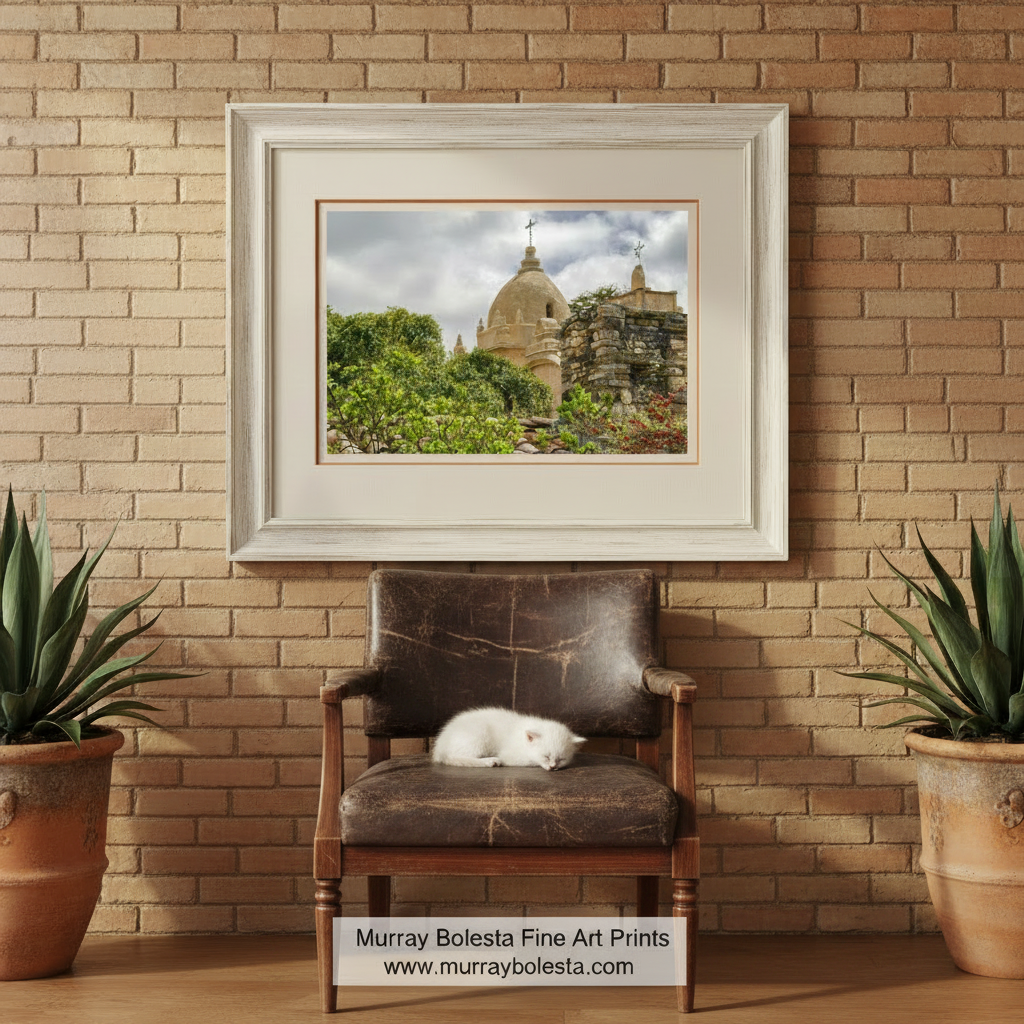 a large, domed building with a cross on top, surrounded by lush greenery and a stone wall. Carmel Mission Church Art Print – Spanish Colonial Architecture Photo by Murray Bolesta