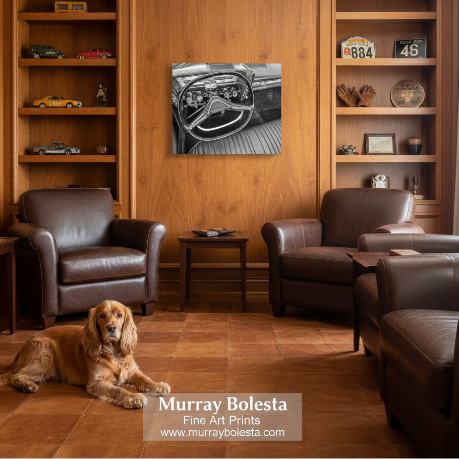 Chrysler Imperial art. A black and white art print of a vintage car dashboard is displayed on a warm wood wall in a cozy living room setting with two brown leather armchairs, a small side table, and a golden dog lying on the floor. A watermark at the bottom reads 'Murray Bolesta Fine Art Prints'.
