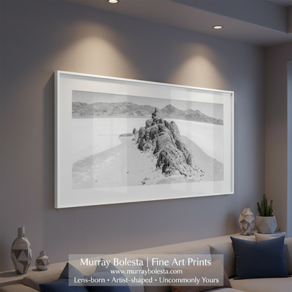 Black and white landscape of a rocky outcrop in a desert with distant mountains. The Racetrack. Black and White Wide Desert Panorama Wall Art with Death Valley National Park by Murray Bolesta