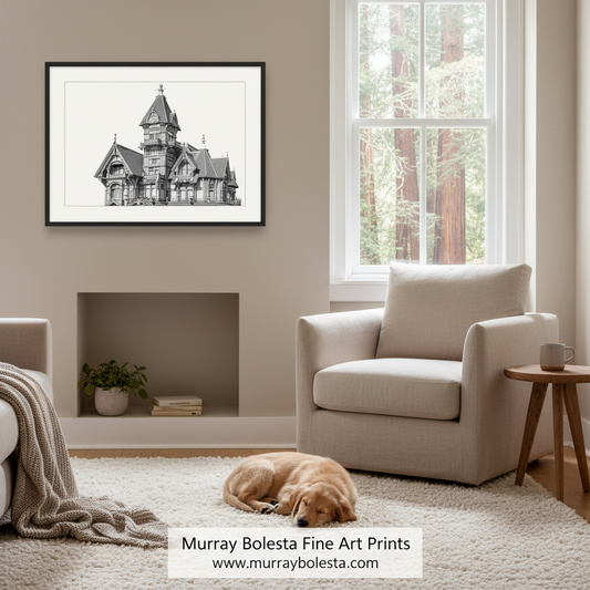 A framed black and white architectural art print of a Victorian-style house is displayed on a beige wall in a modern living room setting with a cream armchair, a sleeping golden dog on the rug, and a window in the background. A watermark at the bottom reads 'Murray Bolesta Fine Art Prints'.