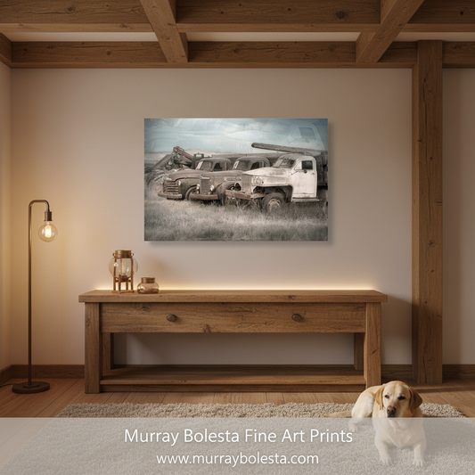 A framed wall art print showing an old white truck in a grassy field, displayed above a wooden console table in a rustic room. A small dog sits on the rug in the foreground, and a floor lamp stands to the left.