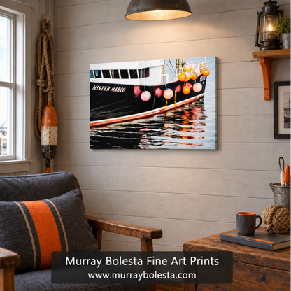 A framed wall art print showing a black fishing boat with orange buoys and colorful reflections in the water, displayed in a styled room setting with a gray armchair, wooden table, and nautical decor. A text overlay at the bottom reads 'Murray Bolesta Fine Art Prints' . Rhode Island boats.