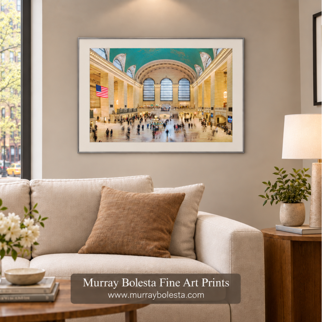 A framed art print of Grand Central Terminal station in New York City, displayed on a beige wall above a light beige sofa in a styled living room setting. The print features a white frame and is presented by Murray Bolesta Fine Art Prints.