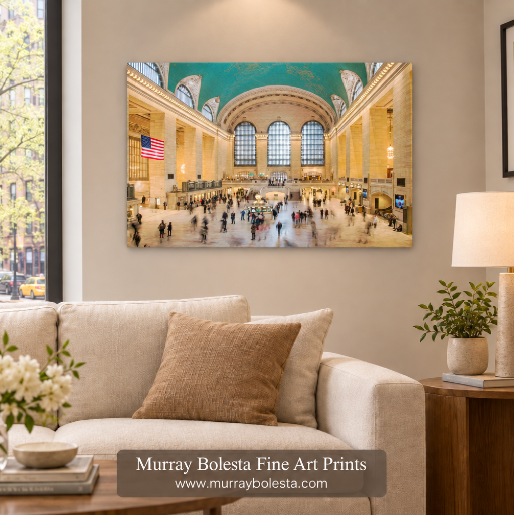 A framed wall art print depicting the grand interior of Grand Central Terminal with a turquoise ceiling and busy floor activity, displayed above a beige sofa in a styled living room. A watermark at the bottom reads 'Murray Bolesta Fine Art Prints' with the website murraybolesta.com