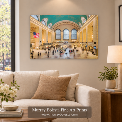 A framed wall art print depicting the grand interior of Grand Central Terminal with a turquoise ceiling and busy floor activity, displayed above a beige sofa in a styled living room. A watermark at the bottom reads 'Murray Bolesta Fine Art Prints' with the website murraybolesta.com