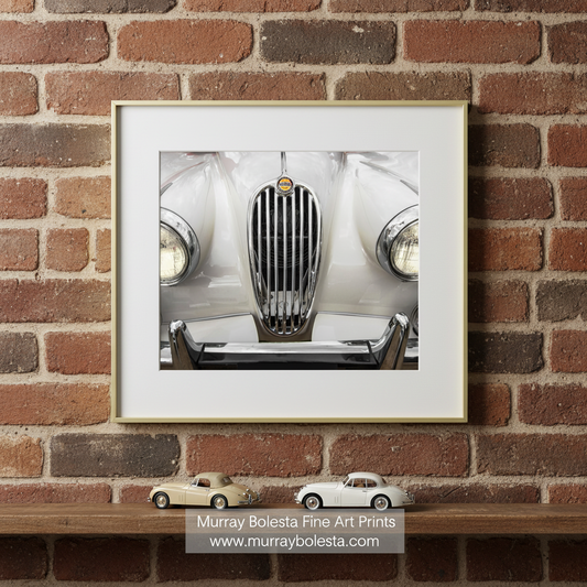 A close-up view of the front end of a classic white car, showcasing its chrome grille and headlights. Classic Jaguar XK140 Car Photograph | English Car Wall Art by Murray Bolesta