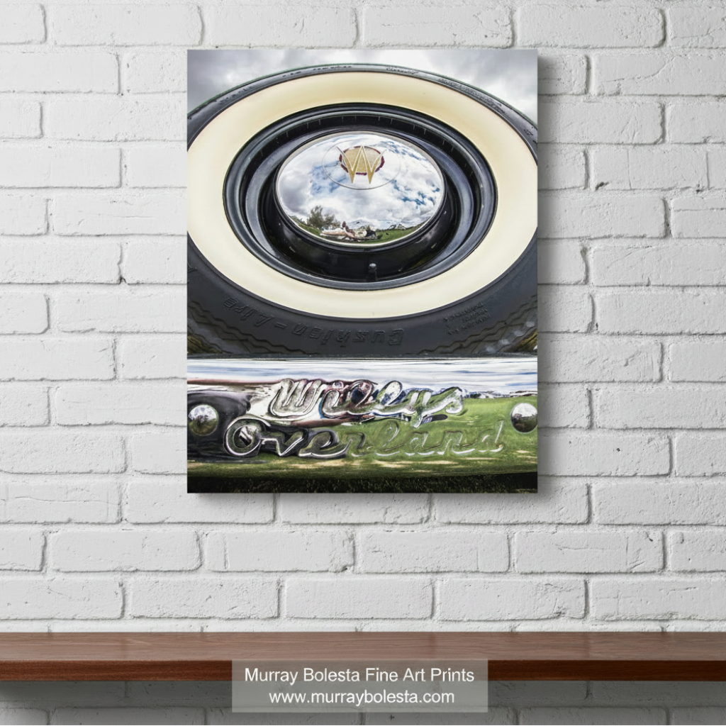 a close-up view of a vintage car's chrome bumper and round headlight, with a reflection of a kite in the center. Willys Overland Jeepster Classic Car Photography Art Print by Murray bolesta