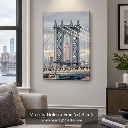 A vertical canvas wall art print depicting the Manhattan Bridge over the water with the New York City skyline, displayed on a light gray wall in a modern living room setting. A watermark banner for 'Murray Bolesta Fine Art Prints' is visible at the bottom.
