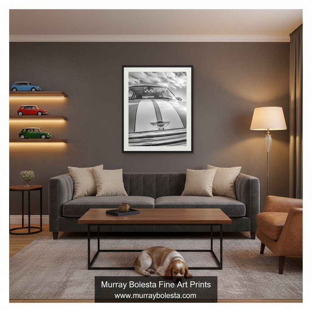 Mini Cooper art by Murray Bolesta. A framed black and white art print of a classic car hanging on a dark gray wall in a modern living room setting with a gray sofa, wooden coffee table, and a dog lying on the rug.