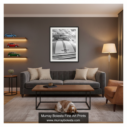 Mini Cooper art by Murray Bolesta. A framed black and white art print of a classic car hanging on a dark gray wall in a modern living room setting with a gray sofa, wooden coffee table, and a dog lying on the rug.