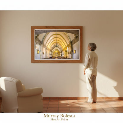 A framed art print depicting a golden archway cathedral interior hangs on a beige wall in a sunlit room, with a person standing in front of it. The text 'Murray Bolesta Fine Art Prints' appears at the bottom.