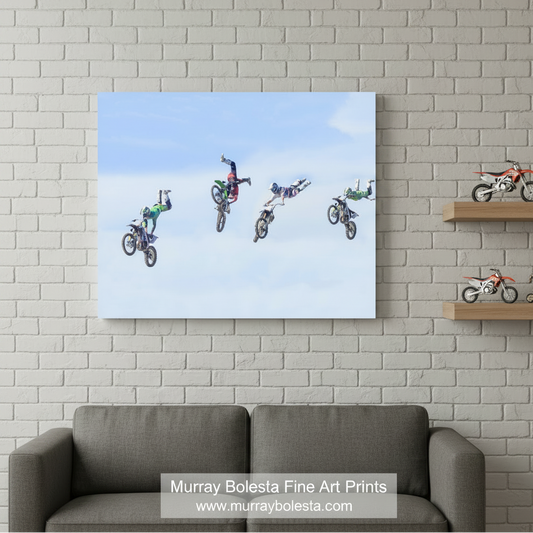 A group of people performing aerial stunts on motorcycles against a blue sky background. Motocross Art Print with Dirt Bikes in Flight | Gift for Biker by Murray Bolesta