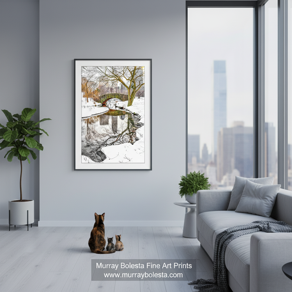 New York Central Park Gapstow Bridge by Murray Bolesta! A framed art print of a snowy park scene with a bridge and trees, displayed on a light gray wall in a modern living room with a sofa, plants, and a cat sitting below the frame.