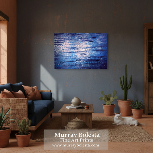 A blue abstract art print depicting water ripples, displayed on a dark gray wall in a styled living room with a blue sofa, wooden table, potted cacti, and a white cat lying nearby. A watermark at the bottom reads 'Murray Bolesta Fine Art Prints'.