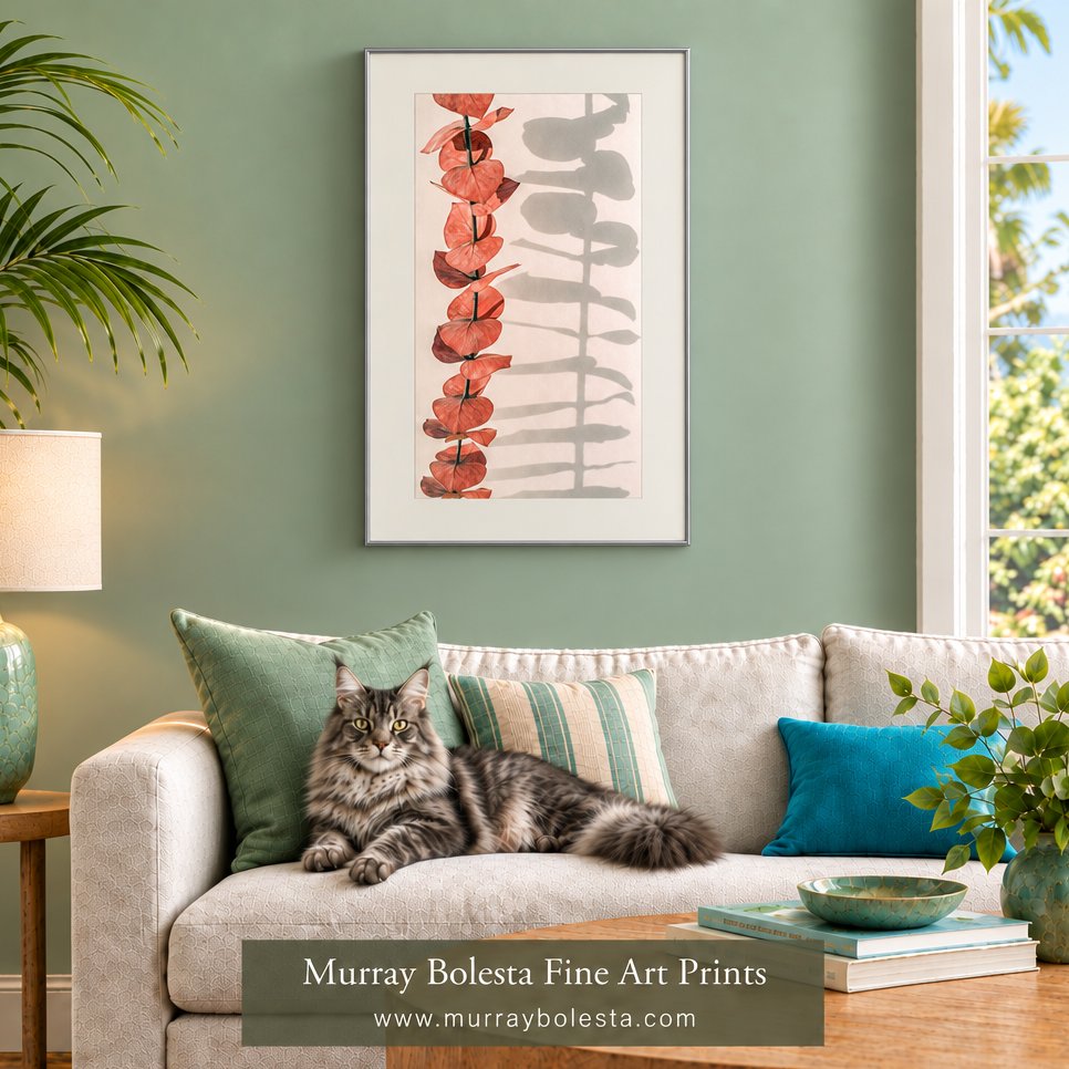 A framed vertical art print hangs on a sage green wall above a beige sofa with a gray tabby cat resting on the couch. The print features a minimalist botanical design with red-orange leaves on the left and gray leaf silhouettes on the right.