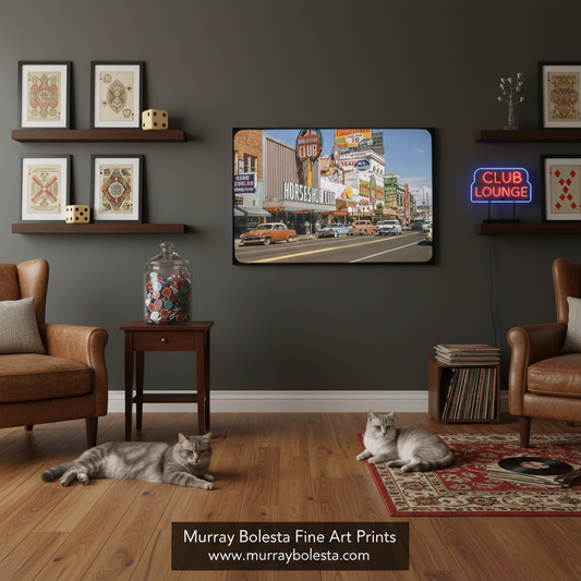 A framed art print depicting a vintage street scene with a 'Club Lounge' neon sign, displayed on a dark gray wall in a styled living room with two cats on a wooden floor.