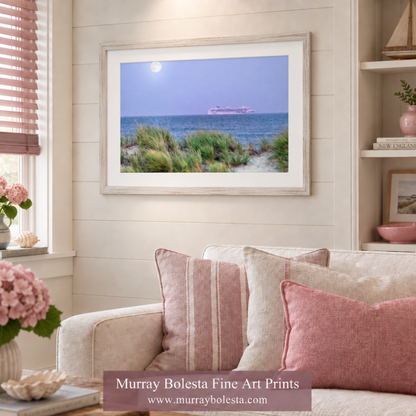 A framed art print of a coastal dune landscape with a cruise ship on the horizon, displayed on a beige shiplap wall above a sofa with pink and beige pillows. A watermark banner for 'Murray Bolesta Fine Art Prints' is visible at the bottom.