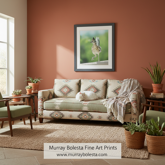 A framed art print of a bird by Murray Bolesta hangs on a terracotta-colored wall above a patterned sofa in a styled living room. The print features a bird in profile against a soft green and blurred background, enclosed in a dark frame.