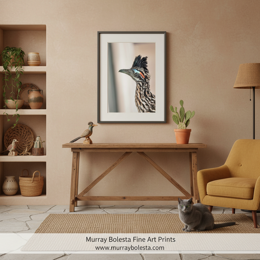 Roadrunner bird by Murray Bolesta. A framed art print of a bird of prey is displayed on a beige wall above a wooden console table in a styled living room setting with a yellow armchair, potted plant, and a gray cat on the floor.
