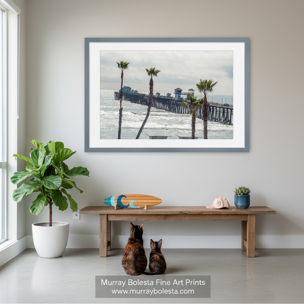 A wooden pier extends into the ocean, with palm trees lining the shoreline in the foreground. Oceanside Pier Print – San Diego Beach Palms Wall Art  by Murray Bolesta!