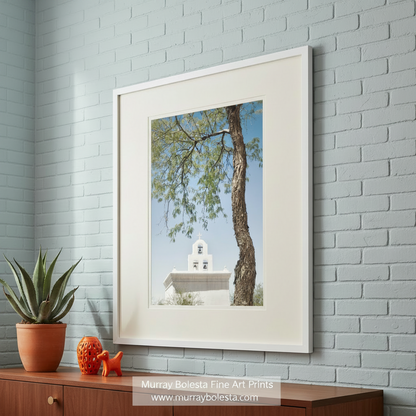 a white bell tower with a cross on top, surrounded by a tree with green leaves and branches. San Xavier Mission Chapel Art - Tucson Arizona Desert Wall Print by Murray Bolesta