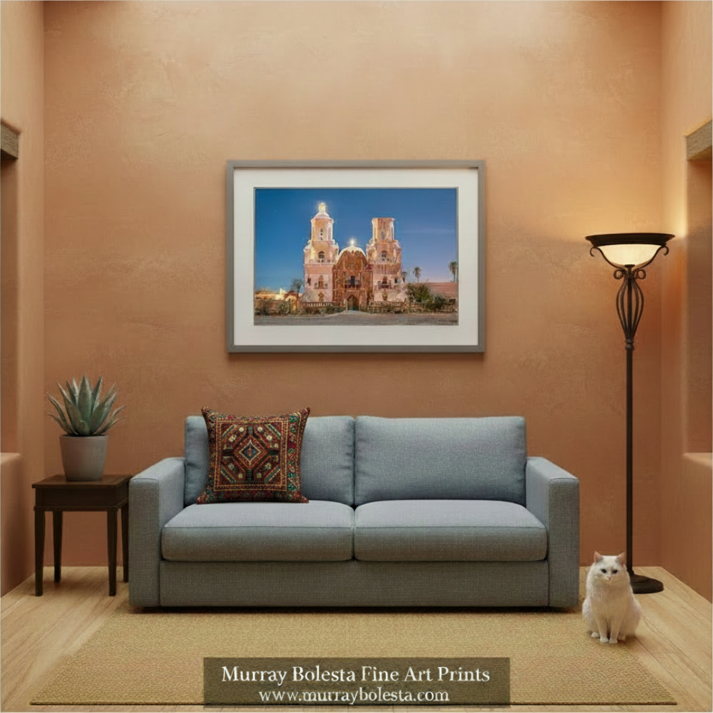 A framed art print of a Spanish-style church in Tucson Arizona displayed on a textured terracotta wall above a light blue sofa in a modern living room setting. The print is from Murray Bolesta Fine Art Prints, as indicated by the text overlay at the bottom.