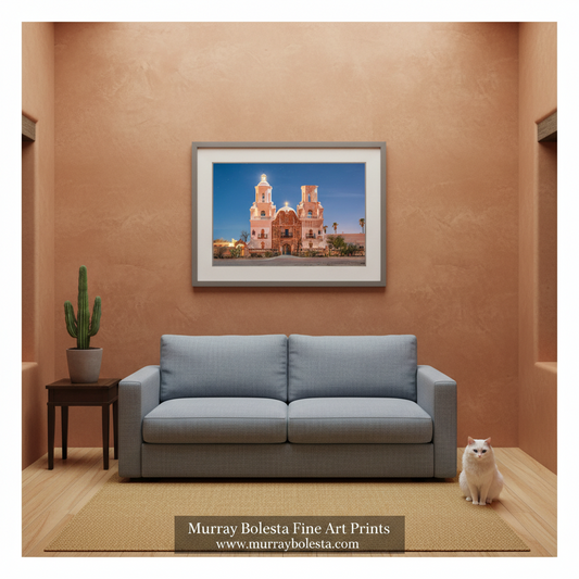 A framed art print of a Spanish-style church in Tucson Arizona displayed on a textured terracotta wall above a light blue sofa in a modern living room setting. The print is from Murray Bolesta Fine Art Prints, as indicated by the text overlay at the bottom.
