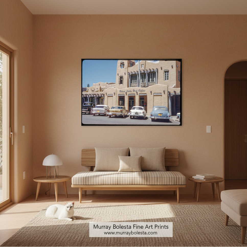 A framed art print depicting a vintage street scene with classic cars and beige buildings, displayed on a warm beige wall above a wooden daybed in a modern, sunlit living room. A watermark at the bottom reads 'Murray Bolesta Fine Art Prints'.
