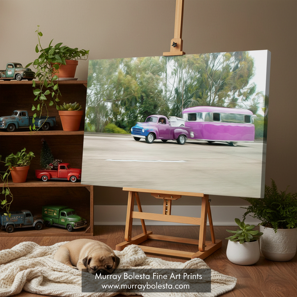 studebaker truck by Murray Bolesta. A canvas art print displayed on a wooden easel in a styled room. The print depicts a vintage purple camper trailer and blue pickup truck on a road with trees in the background.