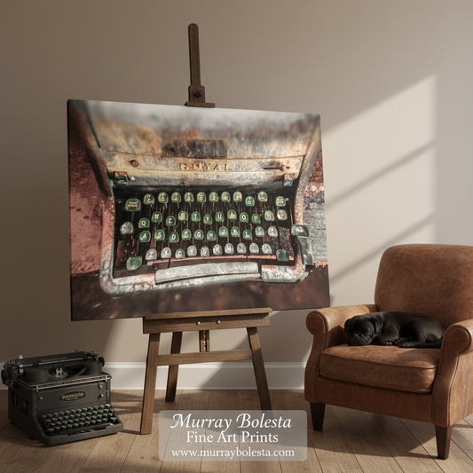 Ghost Writer typewriter. A canvas art print depicting a vintage, rusted typewriter with green keys, displayed on a wooden easel in a styled room setting next to a brown armchair with a sleeping black cat. The text overlay at the bottom reads 'Murray Bolesta Fine Art Prints'.