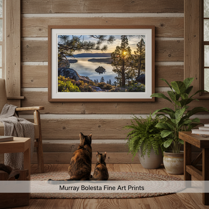 Lake Tahoe artwork! A framed landscape art print of a lake at sunset hangs on a rustic wood-paneled wall above two cats sitting on a rug, with potted plants and furniture in the room. Text at the bottom reads 'Murray Bolesta Fine Art Prints'.