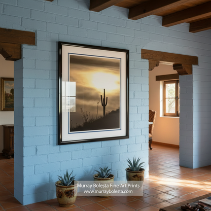 A silhouetted cactus stands against a dramatic sky at sunset, with the sun's rays casting a warm glow over the scene. Desert Sunset Art with Arizona Cactus | Southwestern Decor Print by Murray Bolesta