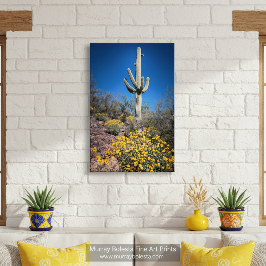 A tall cactus stands in a desert landscape, surrounded by yellow flowers and shrubs against a clear blue sky. Cactus Decor with Spring Desert Flowers | Southwest Design Print by Murray Bolesta