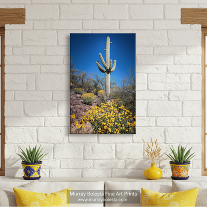A tall cactus stands in a desert landscape, surrounded by yellow flowers and shrubs against a clear blue sky. Cactus Decor with Spring Desert Flowers | Southwest Design Print by Murray Bolesta