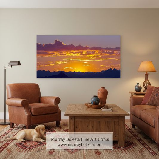 A framed wall art print showing a dramatic sunset over mountain silhouettes, displayed in a styled living room with a brown leather armchair, wooden coffee table, lamp, and a dog on the floor. A watermark at the bottom reads Murray Bolesta Fine Art Prints with the website murraybolesta.