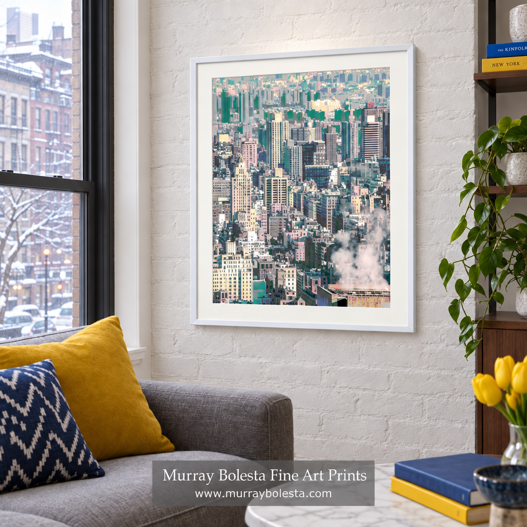 A framed art print of a dense city skyline hangs on a white brick wall in a modern living room setting with a gray sofa, yellow pillows, and a potted plant. NYC winter art by Murray Bolesta.