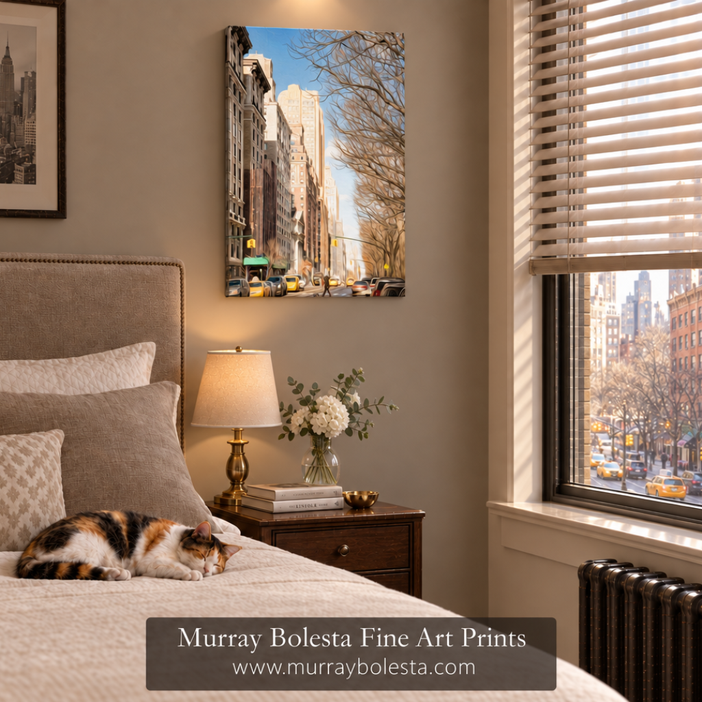 A vertical canvas art print of a New York City street scene hangs on a beige wall above a bed in a styled bedroom. A calico cat sleeps on the bed, and a window with blinds is visible on the right. Art by Murray Bolesta!