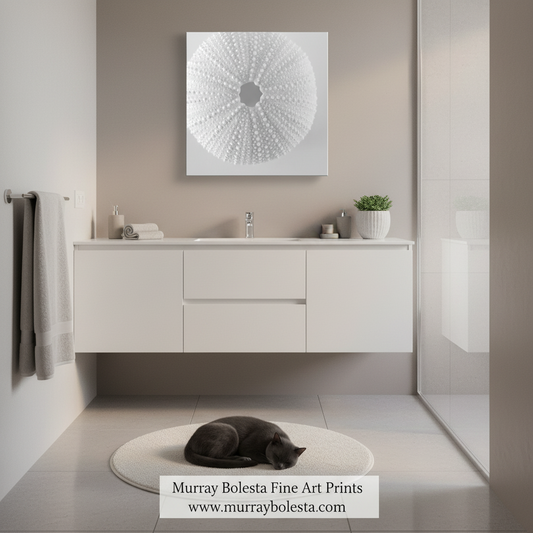 A modern bathroom scene with a white floating vanity, sink, towels, a small plant, and a black cat sleeping on a round rug. Above the vanity hangs a square wall art print with a white circular radial pattern on a light background.