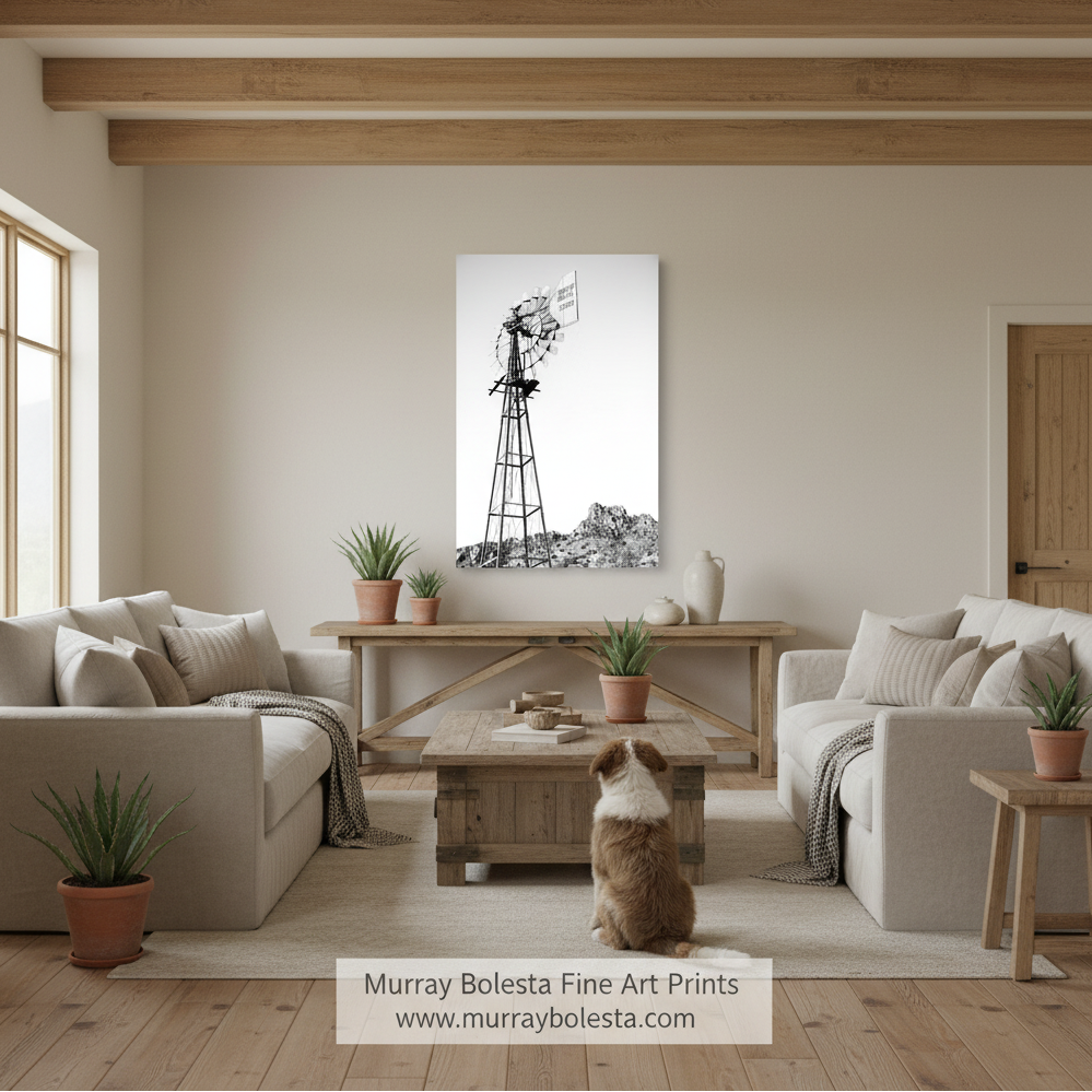 Tucson ranch windmill by Murray Bolesta! A black and white canvas print of a windmill landscape, mounted on a beige wall in a modern, neutral-toned living room with a dog sitting on the floor in front of it.