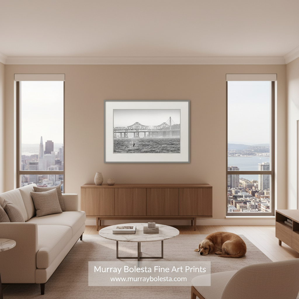A framed black and white fine art print of a bridge over water hangs on a beige wall in a modern living room with a sofa, coffee table, and a sleeping dog on the floor. A watermark at the bottom reads 'Murray Bolesta Fine Art Prints'.
