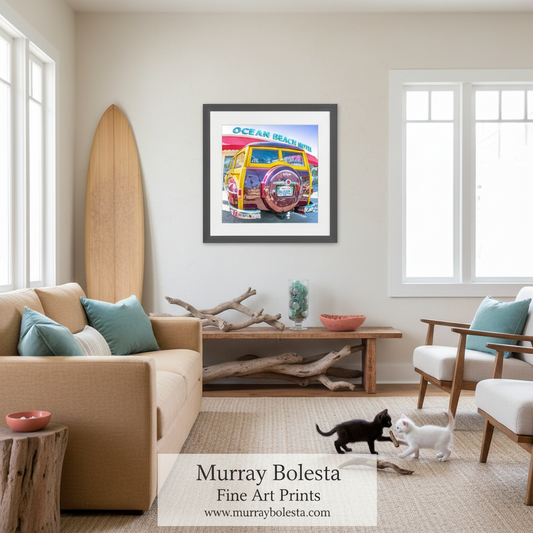 A framed art print titled 'Ocean Beach' featuring a colorful vintage beach car, displayed on a beige wall in a modern, sunlit living room with a sofa, chairs, and two cats on a woven rug.