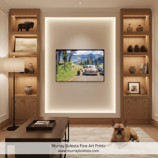 A framed landscape art print depicting a vintage car journey through a scenic mountain valley, displayed on a wall in a modern, warm-toned living room setting with a dog lying on a rug below.